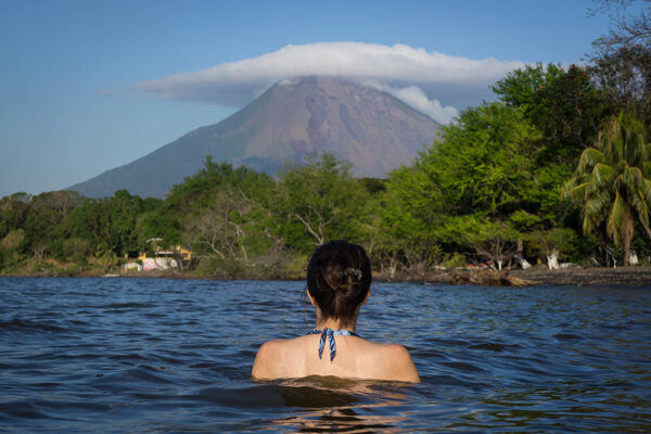 Back view of young woman swimming in Lake Nicaragua with a view of Volcano Concepción on Ometepe Island, Nicaragua