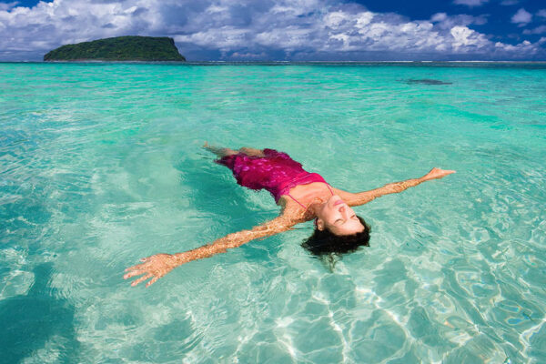 woman in a pink dress floating in the turquoise sea in Samoa